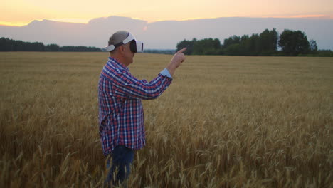 Älterer-Erwachsener-Bauer-In-Einem-Virtual-Reality-Helm-Auf-Einem-Getreidefeld.-Im-Abendlicht-Benutzt-Ein-älterer-Mann-In-Einem-Traktor-Eine-Virtual-Reality-Brille.-VR-Technologien-Und-Moderne-Agrarwirtschaft